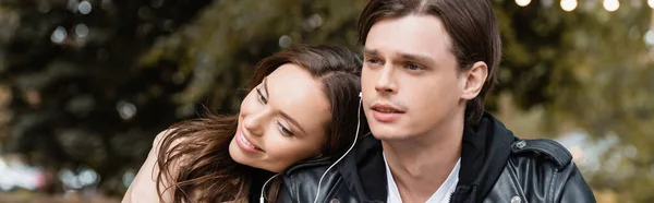 Cheerful woman and young man sharing wired earphones while listening music together, banner — Stock Photo