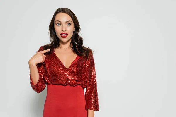 Shocked woman in red dress pointing with finger on grey background — Stock Photo