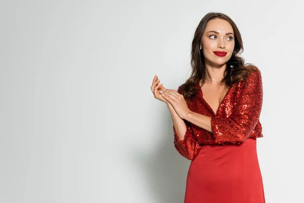 Mujer sonriente en elegante vestido rojo mirando hacia otro lado sobre fondo gris - foto de stock