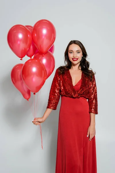 Jeune femme en robe rouge tenant des ballons de fête sur fond gris — Photo de stock