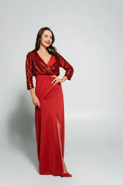 Полная длина модной женщины в красном платье улыбается на сером фоне — стоковое фото