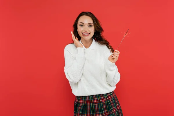 Mujer morena positiva sosteniendo chispeante y mirando a la cámara aislada en rojo - foto de stock