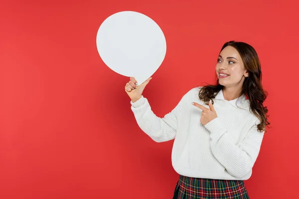 Mujer sonriente en suéter acogedor apuntando a la burbuja del habla sobre fondo rojo - foto de stock