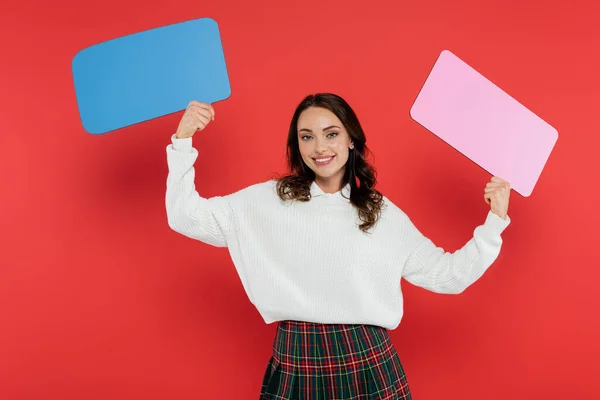 Cheerful woman in cozy sweater holding speech bubbles on red background — Stock Photo