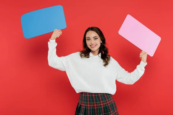 Mujer alegre en suéter acogedor sosteniendo burbujas de habla sobre fondo rojo - foto de stock