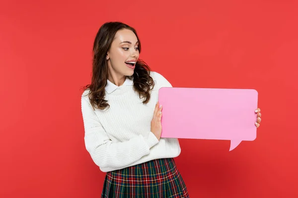 Happy woman in sweater looking at empty speech bubble isolated on red — Stock Photo