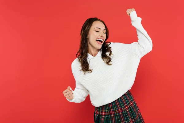 Mujer joven feliz en suéter bailando aislado en rojo - foto de stock