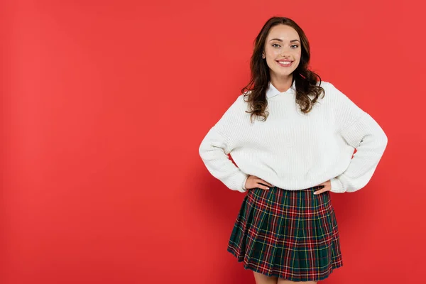 Smiling woman in warm sweater and plaid skirt looking at camera on red background — Stock Photo