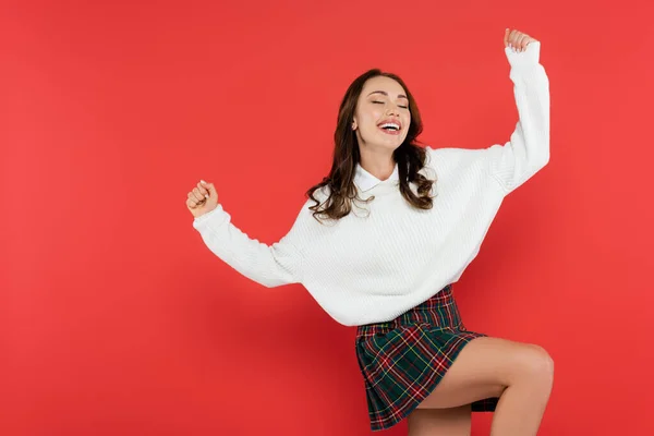 Позитивная девушка в юбке и свитере танцует на красном фоне — стоковое фото
