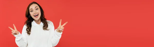 Aufgeregte Frau im weißen Pullover zeigt Siegeszeichen und blickt vereinzelt in die Kamera auf rotem Banner — Stockfoto