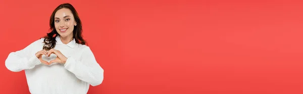 Femme brune positive en pull confortable montrant un signe cardiaque isolé sur rouge, bannière — Photo de stock