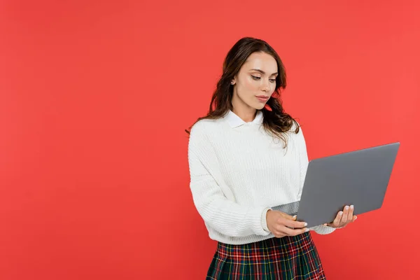 Brunette woman in warm jumper using laptop isolated on red — Stock Photo