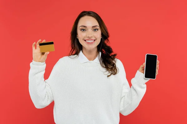 Bella donna bruna in maglione con cellulare e carta di credito isolata su rosso — Foto stock