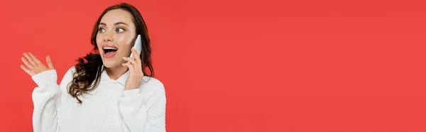 Mujer emocionada en saltador acogedor hablando en el teléfono inteligente aislado en rojo, pancarta - foto de stock