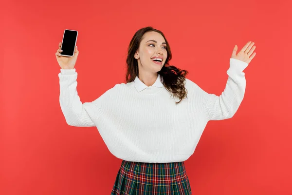 Jovem alegre no acolhedor jumper segurando smartphone isolado no vermelho — Fotografia de Stock