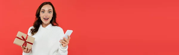 Junge Frau im Pullover mit Geschenk und Handy auf rotem Banner — Stockfoto