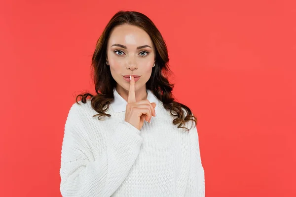 Pretty brunette woman showing secret gesture isolated on red — Stock Photo