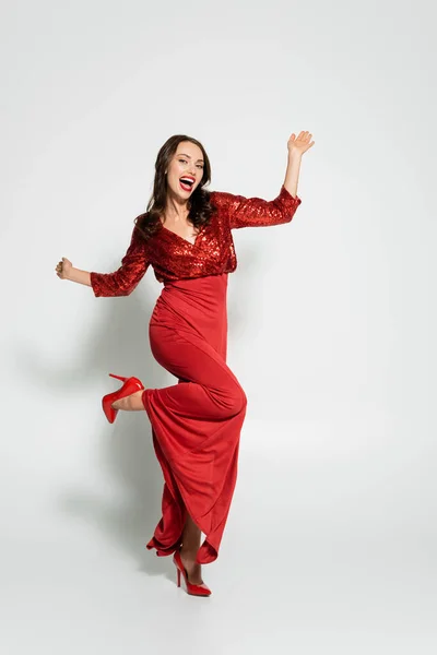 Volle Länge der stilvollen Frau in High Heels und rotem Kleid schaut in die Kamera auf grauem Hintergrund — Stockfoto