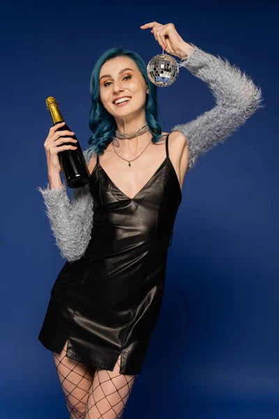 Glückliche Frau im schwarzen Lederkleid mit Champagnerflasche und glänzender Discokugel auf blauem Grund — Stockfoto