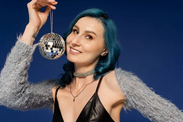 Donna allegra in ecopelle maniche in posa con piccola e lucente palla da discoteca isolata su blu — Foto stock