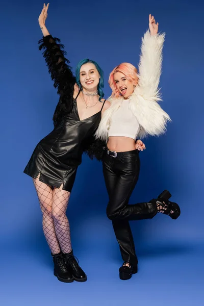 Full length of nonbinary person sticking out tongue while posing with happy friend on blue background — Stock Photo