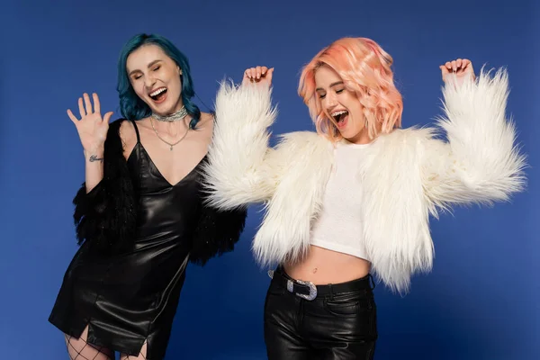 Excited nonbinary people in fluffy faux fur jackets dancing during new year party isolated on blue — Stock Photo