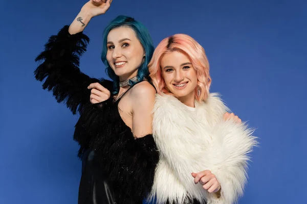 Cheerful nonbinary people in faux fur jackets looking at camera isolated on blue — Stock Photo