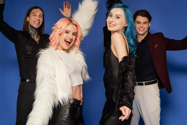 Excited nonbinary person in white faux fur jacket near happy queer friends isolated on blue — Stock Photo