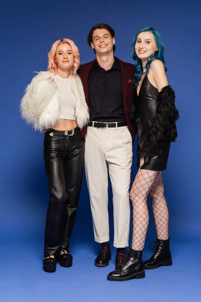 Full length of queer friends in faux fur jackets near nonbinary person in white pants on blue background — Stock Photo