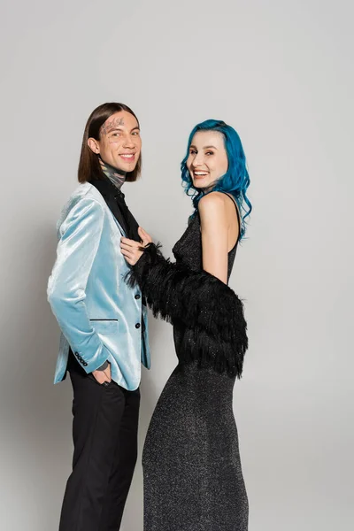 Queer person in blue wig near tattooed nonbinary friend in elegant blazer on grey background — Stock Photo
