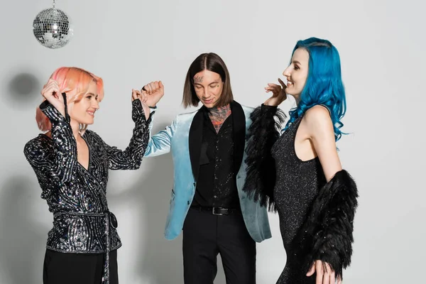 Excited and stylish nonbinary people dancing near tattooed queer friend on grey background — Stock Photo