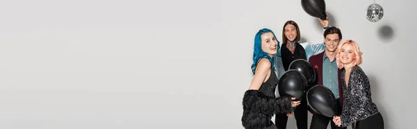 Excited and stylish queer friends holding black balloons on grey background, banner — Stock Photo