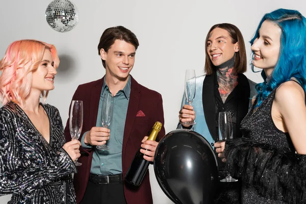 Persona non binaria sorridente con i capelli blu e palloncino nero che celebra il Natale con amici queer su sfondo grigio — Foto stock