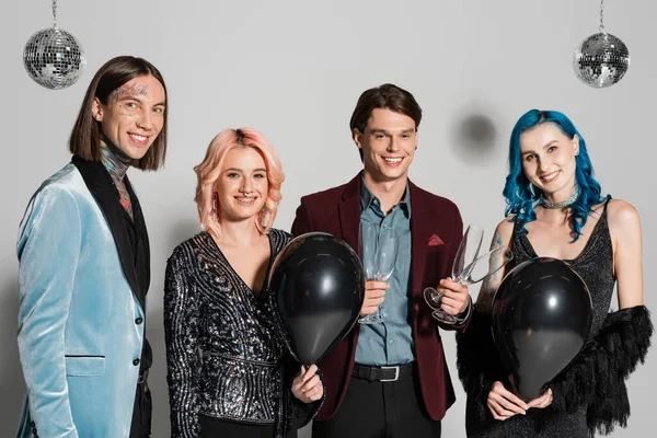 Happy queer people with black balloons and champagne glasses looking at camera on grey background — Stock Photo