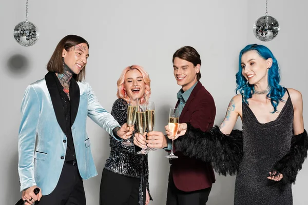 Felices y elegantes amigos queer tintineo copas de champán durante la fiesta de año nuevo sobre fondo gris - foto de stock