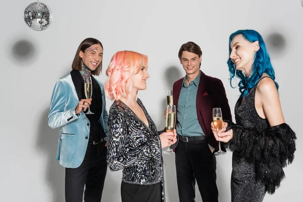 Щасливі небінарні друзі з келихами шампанського посміхаються один одному поблизу квір-людей на сірому фоні — стокове фото