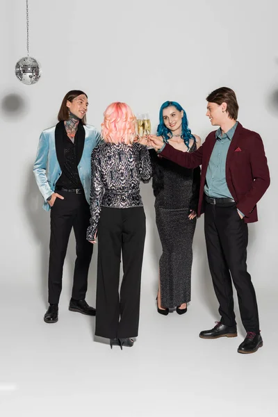 Full length of stylish nonbinary friends clinking champagne glasses on grey background — Stock Photo