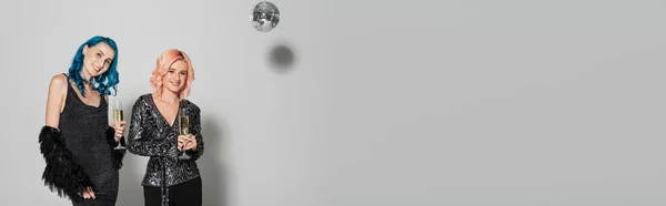 Amis non binaires souriants debout avec des verres de champagne près de la boule de disco sur fond gris, bannière — Photo de stock