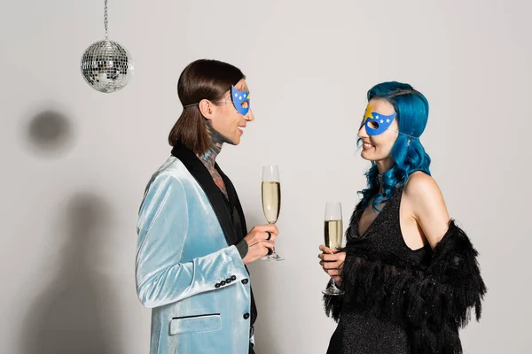 Side view of stylish queer friends holding champagne glasses near disco ball on grey background — Stock Photo