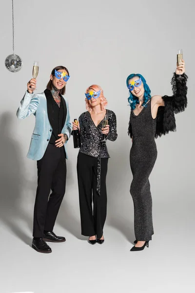Comprimento total de amigos queer elegantes brindar com champanhe e olhando para a câmera no fundo cinza — Fotografia de Stock