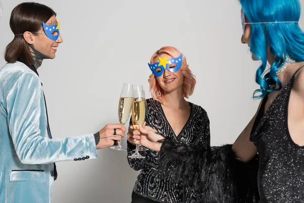 Счастливые голубые люди в масках для вечеринок звонят в бокалы для шампанского во время празднования Рождества на сером фоне — стоковое фото