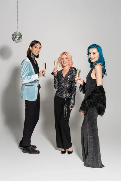 Full length of elegant nonbinary people with champagne glasses celebrating christmas on grey background — Stock Photo