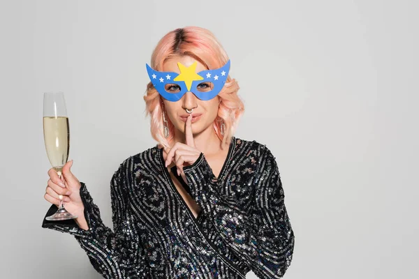 Woman in party mask and elegant blouse showing hush sign while holding champagne isolated on grey — Stock Photo