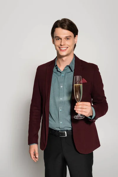 Joven feliz en chaqueta marrón sosteniendo copa de champán aislado en gris - foto de stock