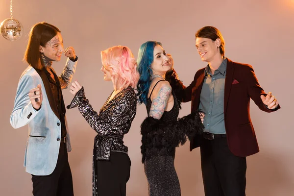 Happy and stylish queer people celebrating christmas and dancing on beige background with pink lighting — Stock Photo