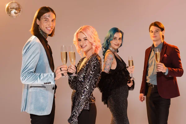 Cheerful queer people in festive and elegant clothes holding champagne while celebrating christmas on beige — Stock Photo