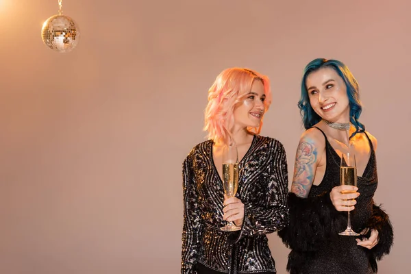 Tätowierte queere Person mit Champagnerglas, die ihren Freund auf beigem Hintergrund ansieht — Stockfoto