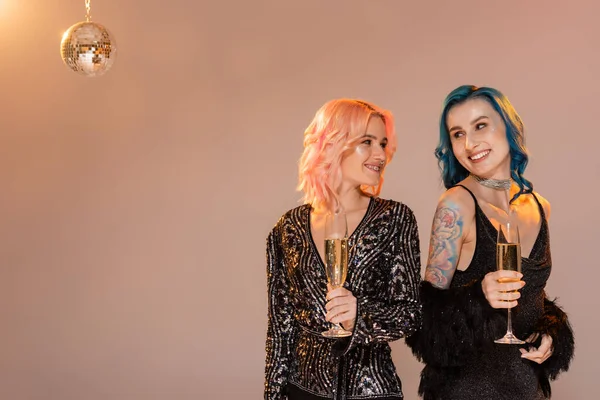 Tattooed queer person with champagne glass looking at friend on beige background — Stock Photo