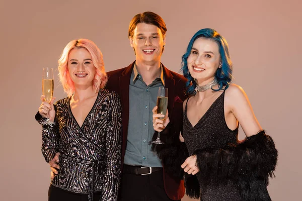 Happy nonbinary people holding champagne glasses near queer friend isolated on beige — Stock Photo
