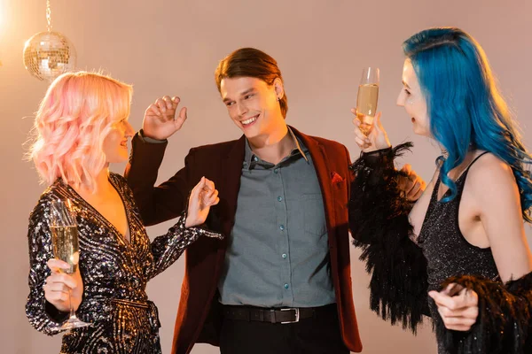 Alegre queer amigos com taças de champanhe dançando perto brilhante bola de discoteca no fundo bege — Fotografia de Stock